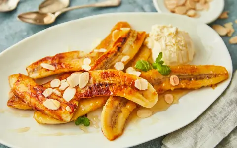 Gebackene Bananen mit einer Kugel Eis, garniert mit Mandelblättchen und Minze. Ein süßer Genuss!