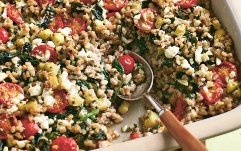 Herzhaftes Gericht mit gekochtem Dinkel, Tomaten, Zucchini und Feta. Ein Löffel hebt die köstliche Mischung aus der Auflaufform.