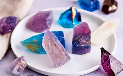 Bunte, essbare Kristalle selber machen: glitzernde Zuckerstücke in Blau, Lila und Weiß mit goldenen Akzenten auf einem Teller.