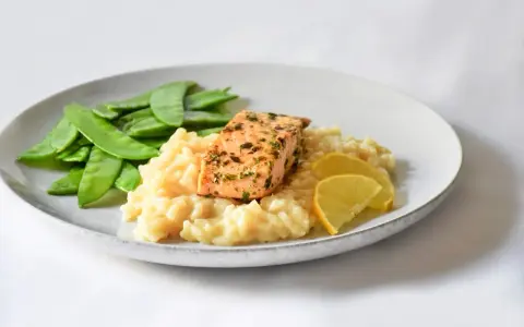 Ein Stück Lachs auf cremigem Zitronenrisotto, garniert mit Zuckerschoten und Zitronenspalten.