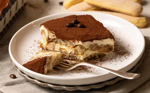 Ein Stück cremiges Tiramisu, bestäubt mit Kakao, wartet auf dich. Dieses Tiramisu Rezept ist ein Genuss!