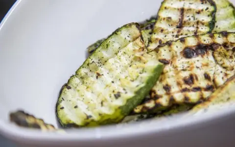 Gegrillte Zucchinischeiben mit Kräutern und Gewürzen in einer weißen Schüssel. Eine köstliche Zucchini Pfanne.