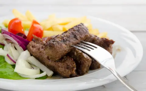 Saftige cevapcici mit knusprigen Pommes, garniert mit frischem Salat, Tomaten und Zwiebeln. Ein köstliches Gericht!