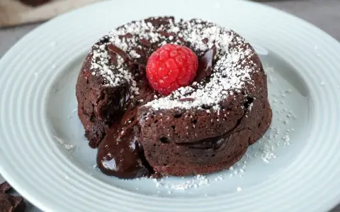 Ein warmer Schokoladenkuchen, ein Coulant de Chocolate, mit flüssigem Kern, garniert mit einer Himbeere und Puderzucker.
