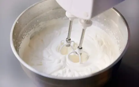 Ein Handmixer schlägt Kochsahne in einer Edelstahlschüssel zu steifer Masse.