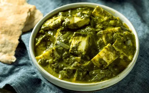 Schüssel mit cremigem Palak Paneer, einem indischen Gericht aus Spinat und Käse, daneben Fladenbrot.