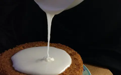 Ein Kuchen wird mit zuckerguss mit milch überzogen. Der flüssige Guss fließt langsam auf die runde Kuchenoberfläche.