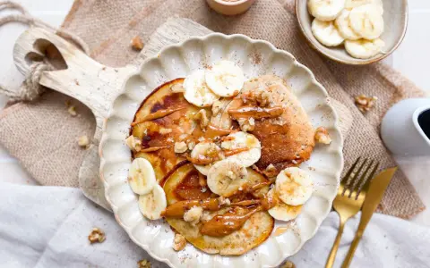 Bananen Pancakes ohne Ei, garniert mit Bananenscheiben, Nüssen und einer cremigen Sauce. Ein köstlicher Brunch-Traum!