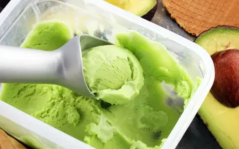Cremiges, grünes veganes Eis, perfekt zum veganes Eis selber machen mit Mandelmilch. Avocados und Waffeln im Hintergrund.