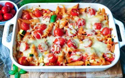 Ein köstlicher nudelauflauf vegetarisch mit Penne, Kirschtomaten und geschmolzenem Käse in einer weißen Auflaufform.