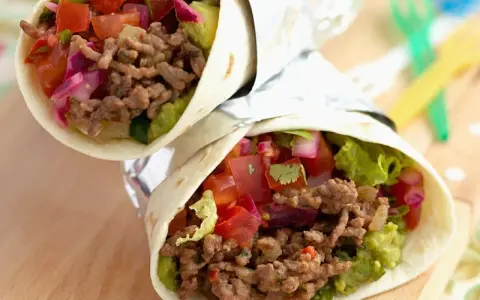 Zwei leckere wraps mit hackfleisch, Guacamole, Tomaten und roten Zwiebeln, eingewickelt in Folie.