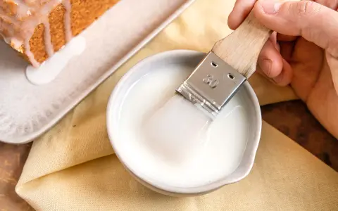 Ein Pinsel taucht in eine Schüssel mit zuckerguss, bereit, einen warmen oder kalten Kuchen zu verfeinern.