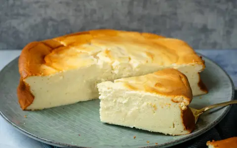 Ein saftiger Quarkkuchen ohne Boden, goldbraun gebacken, liegt auf einem Teller. Ein Stück ist bereits angeschnitten.