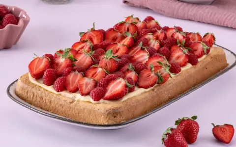 Ein rechteckiger Biskuit-Erdbeerkuchen vom Blech, üppig belegt mit frischen Erdbeeren und Himbeeren auf einer cremigen Schicht.