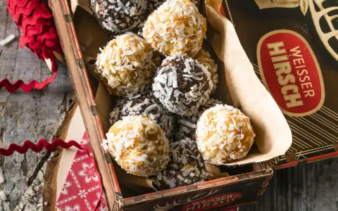 Leckere energy balls selber machen! Eine Mischung aus dunklen und hellen Kugeln, umhüllt von Kokosraspeln, in einer alten Blechdose.