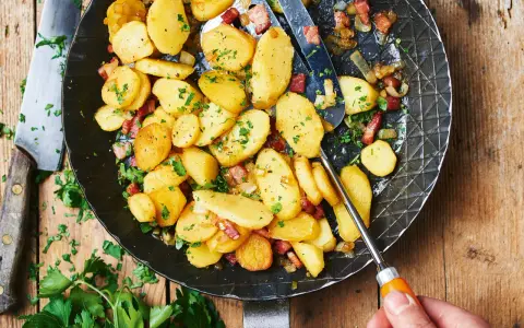 Bratkartoffeln mit mehligen Kartoffeln, Speck und Zwiebeln in einer Pfanne, garniert mit Petersilie.