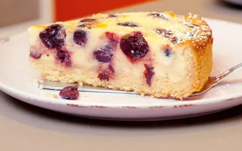 Ein Stück Kirsch-Schmand-Kuchen, wie ihn Landfrauen backen, mit saftigen Kirschen und Puderzucker bestäubt.