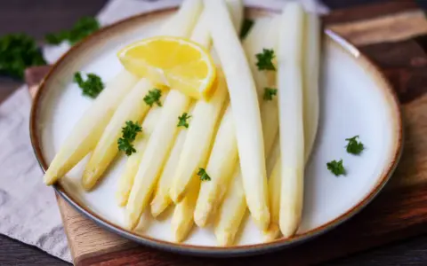 Frischer weißer Spargel, perfekt gegart, liegt auf einem Teller, garniert mit Petersilie und einer Zitronenspalte.