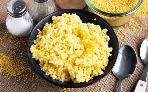 Goldhirse kochen: Ein Teller mit dampfender Hirse, daneben Salz- und Pfefferstreuer, Löffel und eine Schüssel voller ungekochter Hirse.