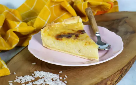 Ein Stück cremiger Milchreiskuchen auf rosa Teller, daneben roher Reis. Ein leckeres Milchreiskuchen Rezept zum Nachbacken.