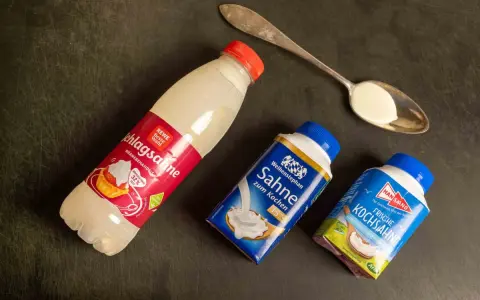 Schlagsahne zum Kochen: verschiedene Sahne-Produkte liegen neben einem Löffel mit Sahne.