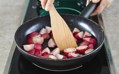 Schnittradieschen werden in einer Pfanne mit einem Holzspatel gewendet.