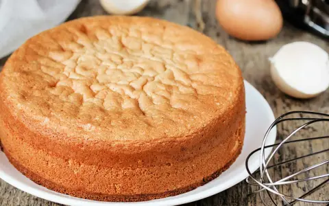 Ein goldbrauner Biskuitboden, perfekt für jedes biskuitboden rezept. Eier und Schneebesen deuten auf die Zubereitung hin.