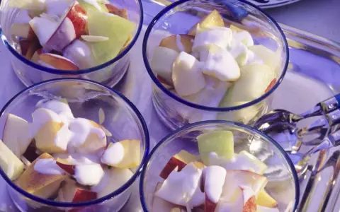 Vier Gläser mit einem erfrischenden Nachtisch mit griechischem Joghurt und Obststücken.