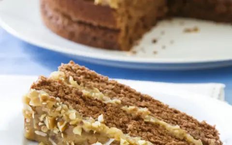 Ein Stück saftige Nusstorte mit cremiger Buttercreme und gehackten Nüssen, bereit zum Genießen.