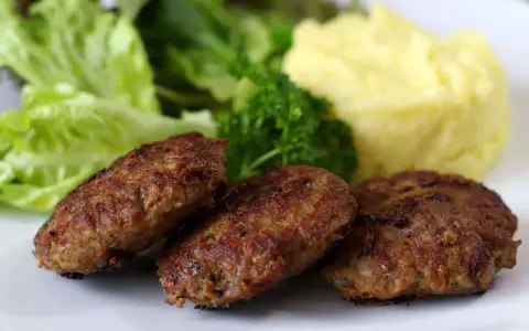 Drei goldbraune Fleischpflanzerl liegen auf einem Teller neben Kartoffelbrei und Salat. Ein leckeres Fleischpflanzerl Rezept zum Nachkochen.