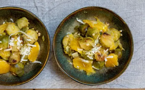 Zwei Schalen mit Rosenkohl, Orangenstücken und geriebenem Käse. Ein Gericht, das an ewiger Kohl Rezepte erinnert.