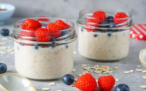 Zwei Gläser mit Overnight Oats, garniert mit frischen Himbeeren und Blaubeeren. Perfekt für ein gesundes Frühstück.