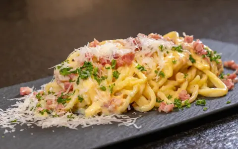Ein Teller cremiger Spaghetti Carbonara, garniert mit Speckwürfeln, Petersilie und frisch geriebenem Parmesan.
