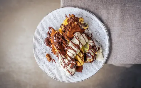 Ein köstlicher Somlauer Nockerl-Dessert auf einem Teller, mit Schokoladensauce und Eiscreme garniert.