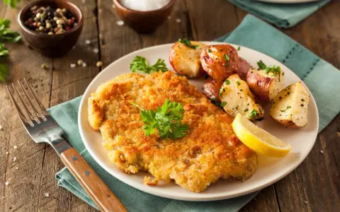 Goldbraunes Schnitzel, perfekt paniert, mit Rosmarinkartoffeln und Zitrone auf einem Teller.