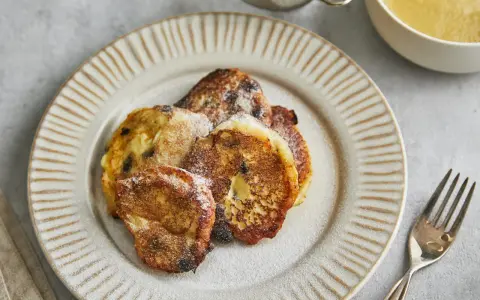 Goldbraune Quarkkeulchen mit Zucker bestreut auf dunklem Teller, daneben Apfelmus und Besteck.