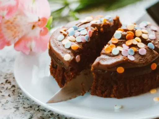 Schokoladenkuchen mit bunter Streusel-Deko, ein köstliches Dessert, um Kuchenreste zu verwerten. Daneben zarte rosa Blüten.
