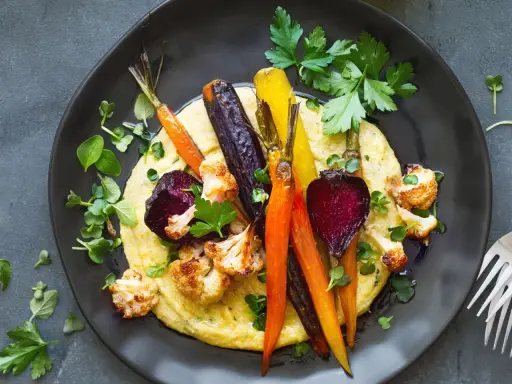 Bunte Wurzelgemüse und Blumenkohl auf cremiger Polenta – eine köstliche Idee, was passt zu Polenta vegetarisch.