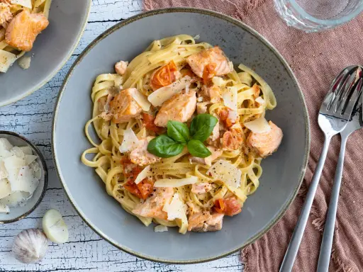 Tagliatelle al salmone mit Kirschtomaten und Parmesan, garniert mit Basilikum. Ein köstliches Gericht, das Lust auf mehr macht.