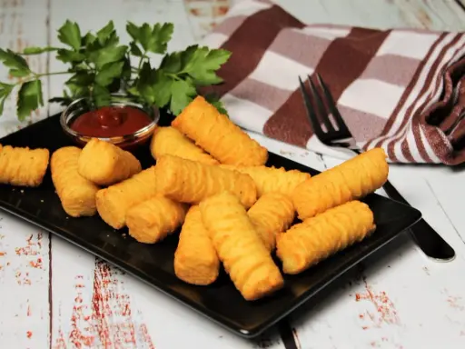 Goldbraune Kroketten, frisch zubereitet, liegen auf einem schwarzen Teller. Dazu gibt es Ketchup und frische Petersilie. Perfekt zum kroketten selber machen!