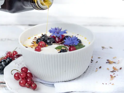Joghurt mit Beeren und leinsamen, beträufelt mit Honig. Blaue Kornblumen zieren die Schüssel.
