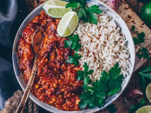 Herzhaftes Chili sin Carne mit Kidneybohnen, Reis, Limettenspalten und Petersilie. Ein Löffel wartet schon.