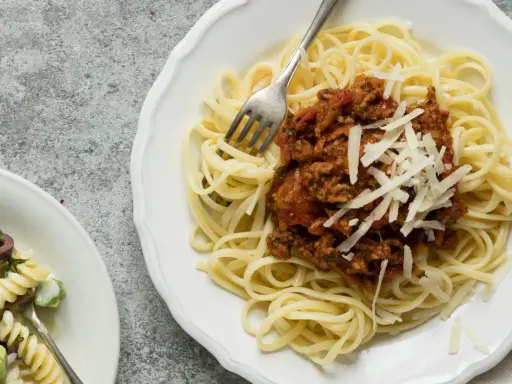 Ein Teller Spaghetti Bolognese, wie nach Omas Rezept, mit frisch geriebenem Parmesan. Daneben ein kleinerer Teller mit Nudelsalat.