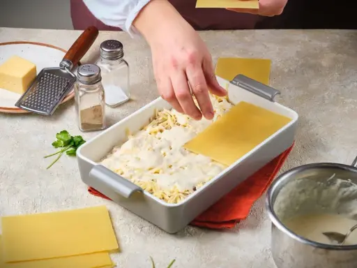 Hände legen Lasagneplatten auf eine Schicht Käse und Sauce. Ein Schritt im Lasagne rezept.