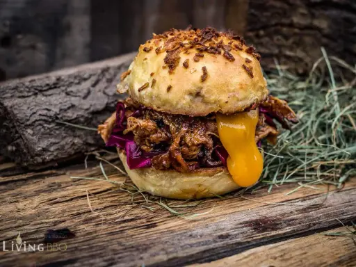 Saftiger pulled chicken burger mit geschmolzenem Käse und Rotkohl auf rustikalem Holz.