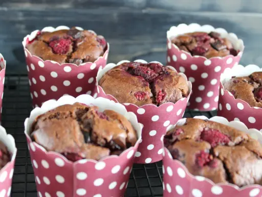 Saftige schokomuffins mit Himbeeren, gebacken in rot-weißen Pünktchen-Förmchen, warten auf ihren Genuss.
