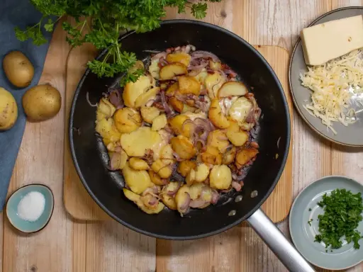 Bratkartoffeln mit Zwiebeln und Käse in der Pfanne. Man muss bratkartoffeln vorher kochen, damit sie schön knusprig werden. Dazu gibt es frische Petersilie und Salz.