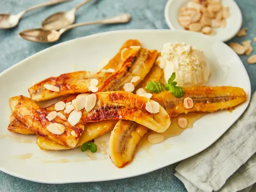 Gebackene Bananen mit einer Kugel Eis, garniert mit Mandelblättchen und Minze. Ein süßer Genuss!