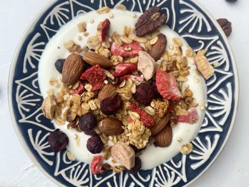 Schüssel mit Joghurt, selbstgemachtem Crunch, Mandeln, gefriergetrockneten Erdbeeren und Blaubeeren.