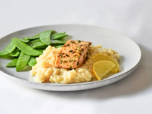 Ein Stück Lachs auf cremigem Zitronenrisotto, garniert mit Zuckerschoten und Zitronenspalten.